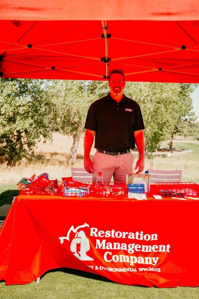 Man standing behind a red table, under a red tent.  