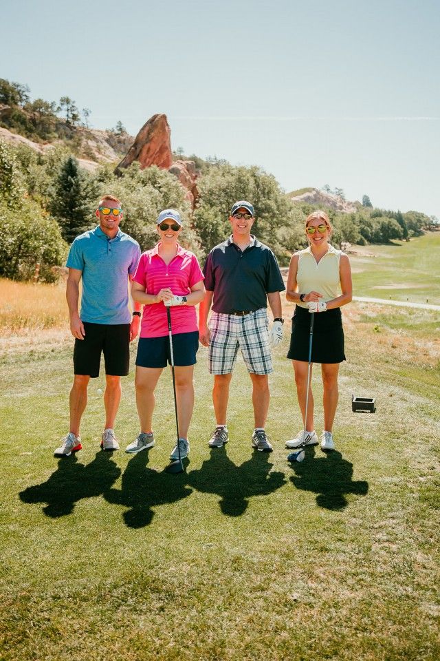 Four people standing on a golf course tee, sunny day, shadows.