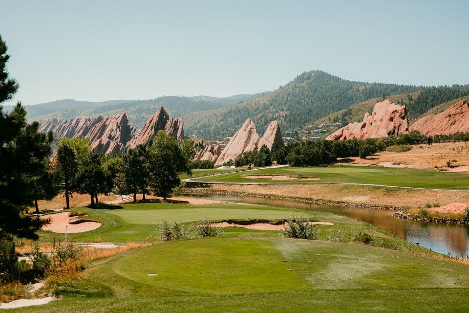 Green golf course with red rock formations and mountain backdrop on a sunny day.