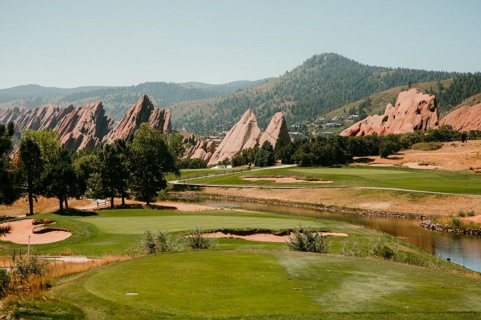 Golf course with reddish rock formations and mountains in the background under a blue sky.