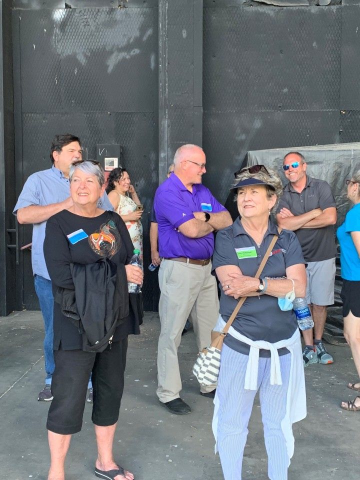 Group of people standing in front of a dark wall, some with arms crossed, looking in different directions.