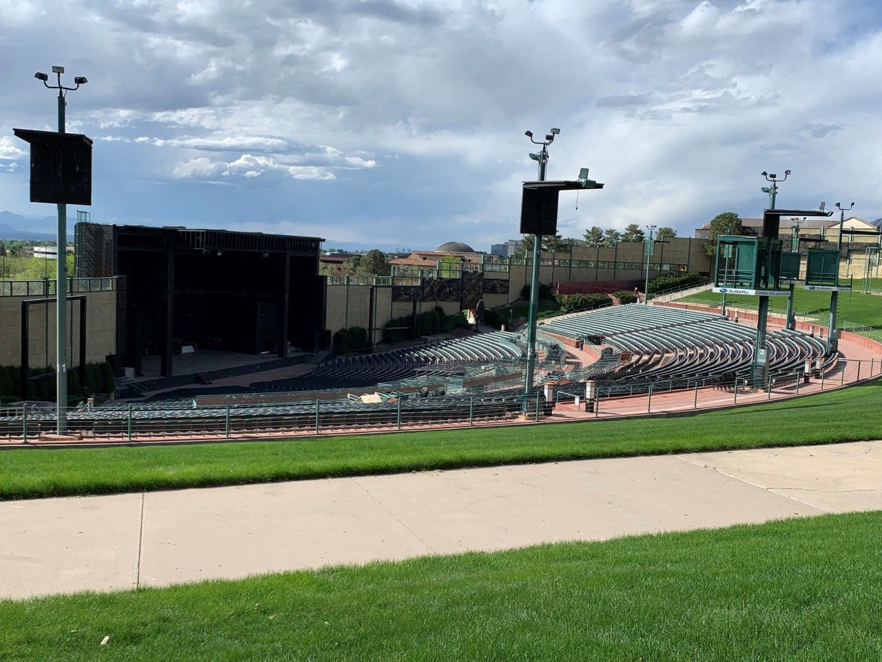 Outdoor amphitheater with rows of seats facing a stage, set against a cloudy sky.