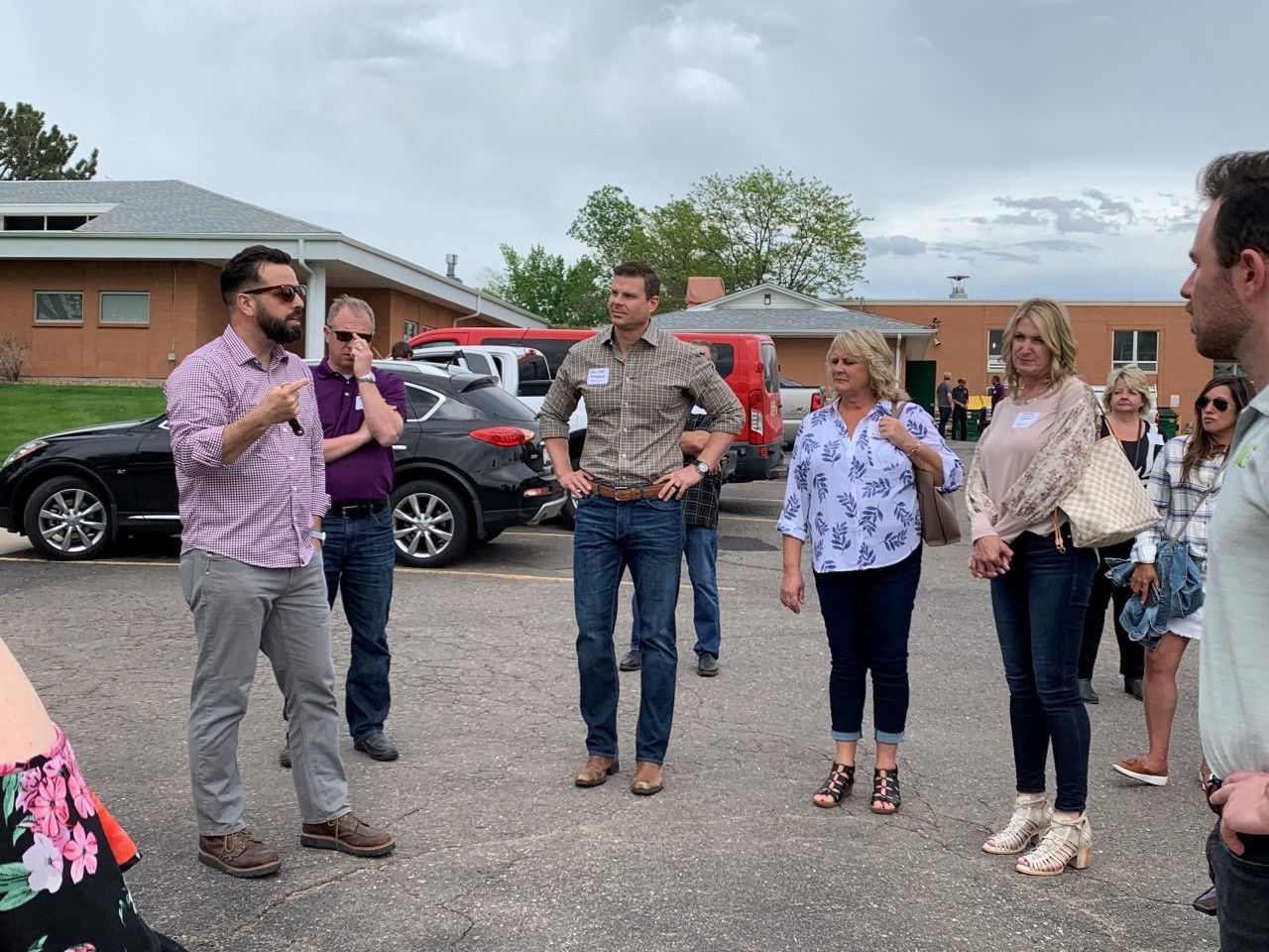 A group of people standing outside; one man in a flannel shirt is the focus. Other people are looking at him.