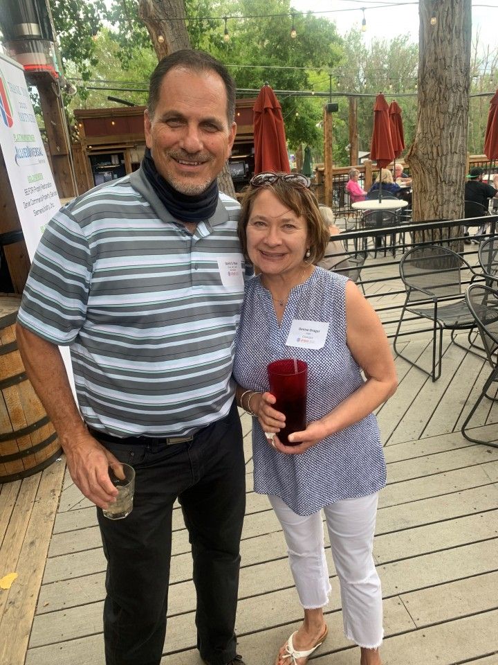 Man and woman on a patio, smiling and posing for a photo. Man in striped shirt, woman in blue and white top.