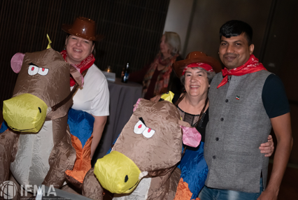 Three people in cowboy attire pose, two with inflatable horse costumes, indoors with a gray backdrop.