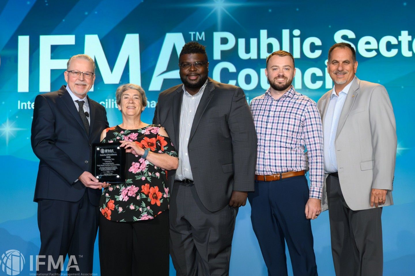 Five people holding an award on a stage with a blue backdrop that says