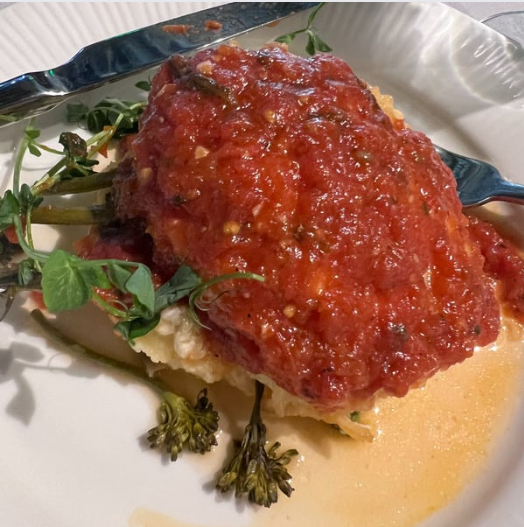 Chicken in tomato sauce with side of greens on a white plate.