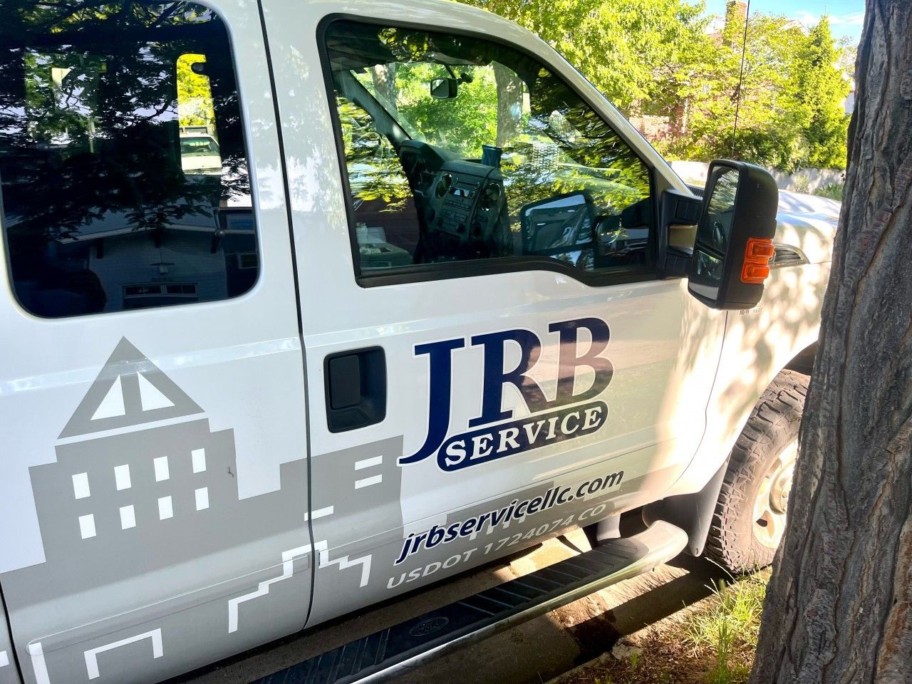 White service truck with JRB SERVICE logo parked next to a tree.
