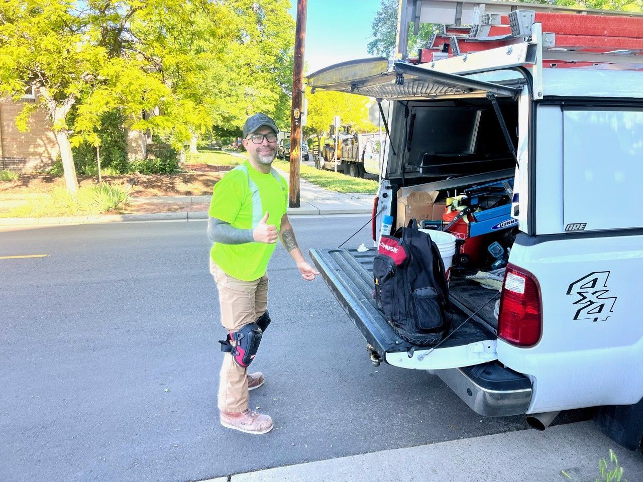 Man in safety vest by a truck with open tailgate, holding a thumb up. Tools visible in the truck.
