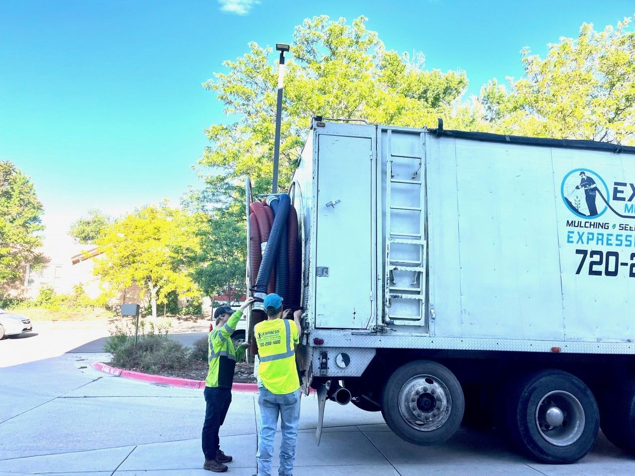 Two people loading items into a white truck with a blue logo, outdoors.