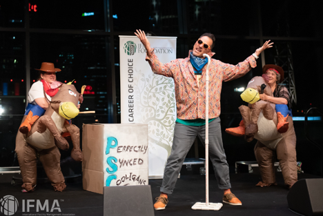 Three people on stage, one singing with a mic, two riding stuffed horse costumes, banner: Career of Choice.