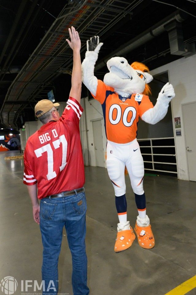 Person in red jersey high-fives the Denver Broncos mascot in a hallway.