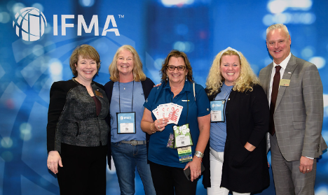 Group of people posing for a photo in front of an IFMA backdrop, one holding giveaway items.