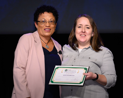 Woman in pink jacket presents certificate to woman in gray shirt.