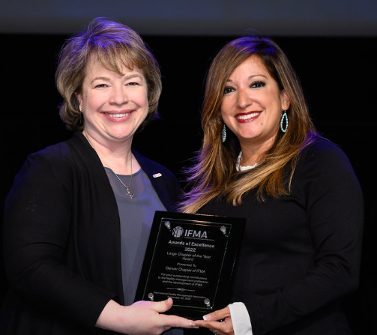 Two women holding an award, smiling. One in black blazer, other in black dress.