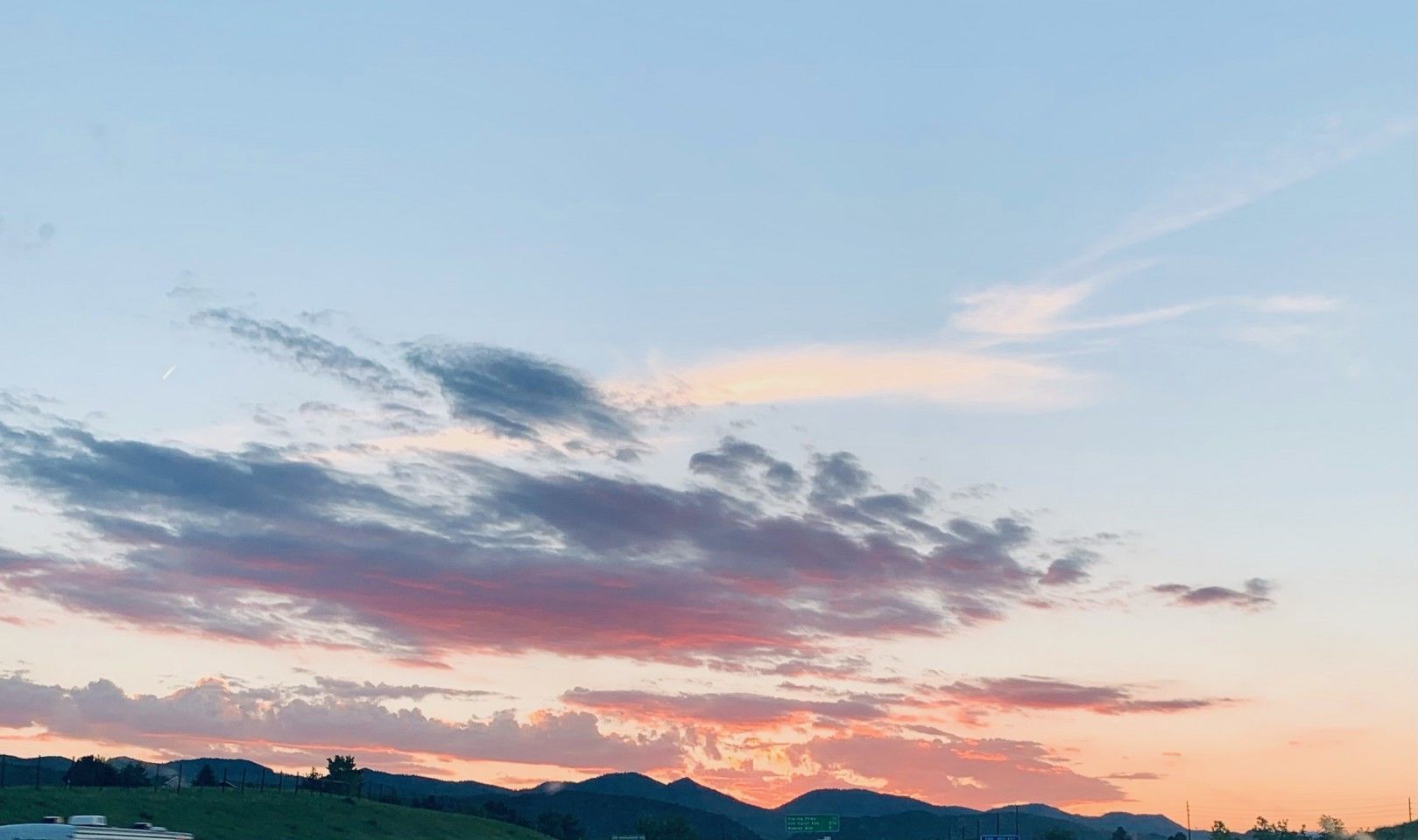 Sunset sky with pink, orange, and blue hues, clouds, and a silhouette of hills.