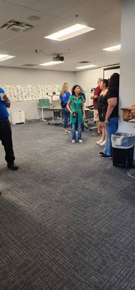 People standing in a room, some looking upward. White walls, carpeted floor, overhead lights.
