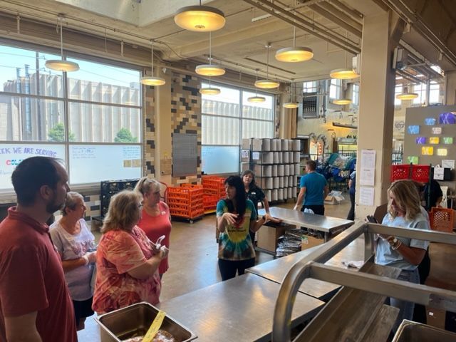People in a brightly lit industrial space, possibly a tour. They are looking at or talking to each other.