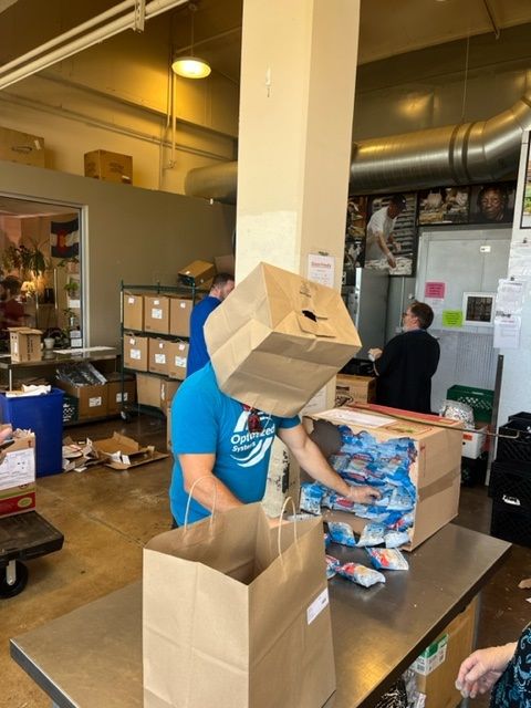 Person with a paper bag on their head helping pack items on a counter, likely at a donation center.