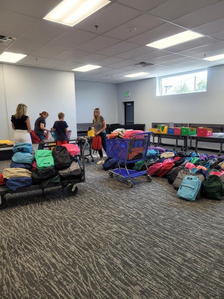 People organizing backpacks and school supplies in a room, likely for donation.