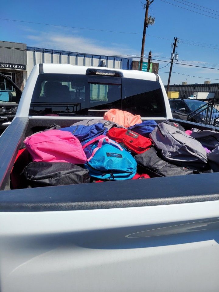 Back of a white truck bed filled with colorful backpacks.