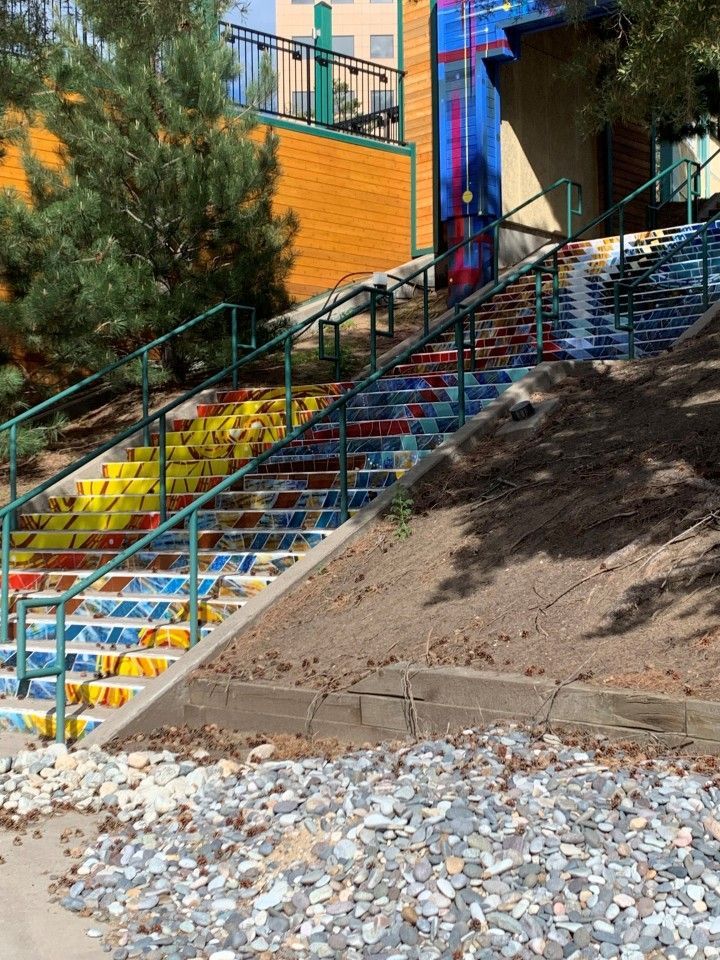 Colorful mosaic-tiled staircase with green handrails ascends hillside next to a building.