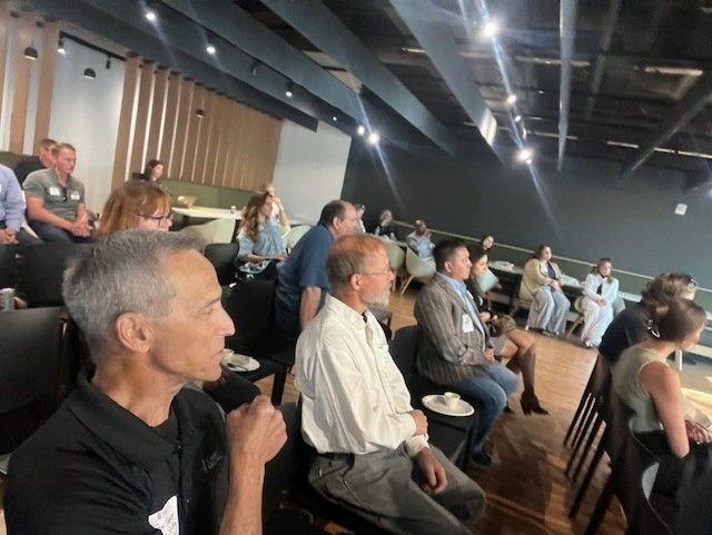 Audience seated, listening attentively at a presentation. Modern setting with wood and neutral-toned walls.