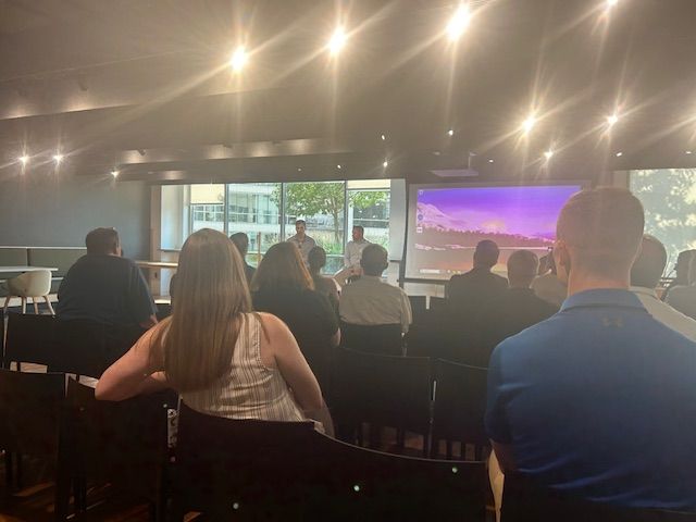 People in chairs attending a presentation; screen shows landscape.
