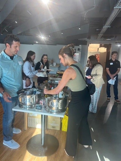 People at a buffet table, selecting food from silver chafing dishes in a brightly lit room.