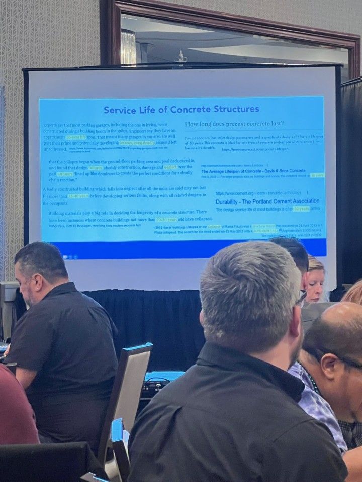 People in a conference hall; a projector screen displays the title 