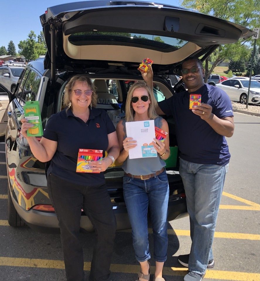 Three people holding food items by an open SUV. Outdoors, sunny.