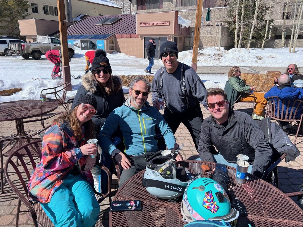 Group of people at outdoor cafe table, snow in background.