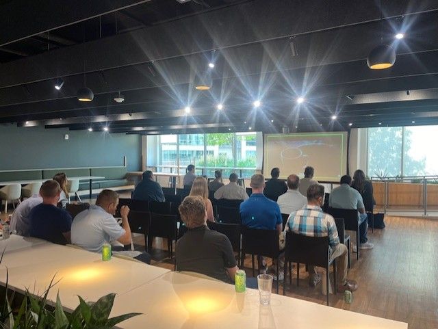 Group of people attending a presentation in a modern office space, focused on a screen.