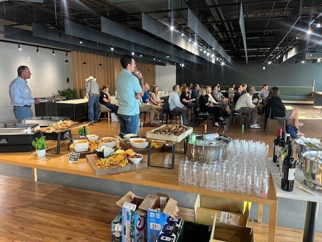 People at an event with food and drinks. Speakers address an audience in a modern open space.