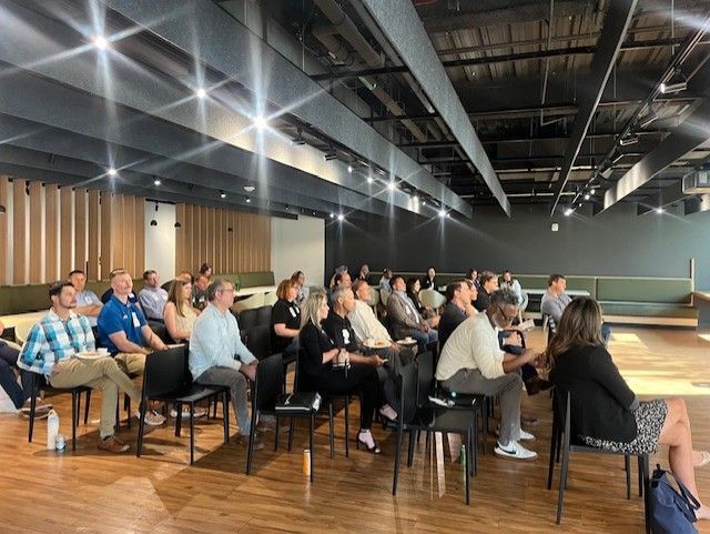 Audience seated, facing a presentation space. People are attending a meeting in a modern room.