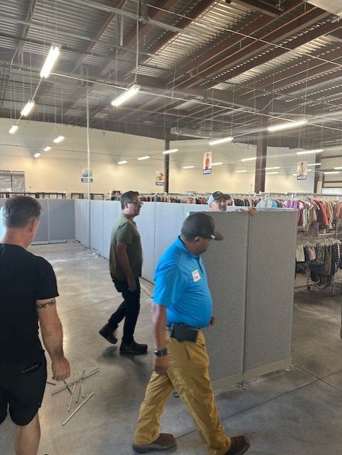 People walking through a large store with gray cubicle walls; fluorescent lights overhead.