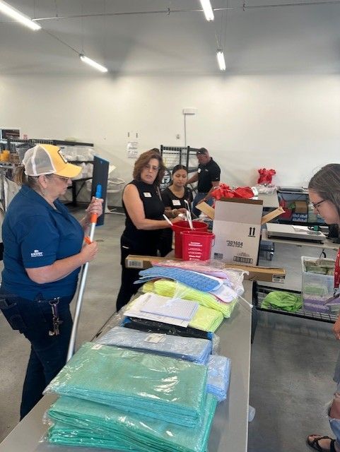 People organizing cleaning supplies in a warehouse; woman holding a squeegee, multiple stacked microfiber cloths.