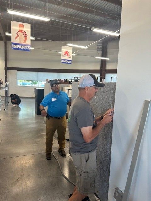 Two men inside a store: one installs panel, other watches. Signs hang from ceiling.