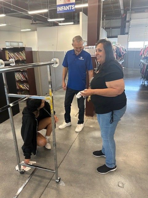 Three people inspecting a rolling clothes rack inside a retail store.