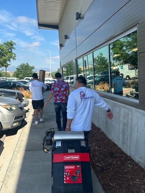 Three people walking next to a building, one carrying a box, another a tool box.
