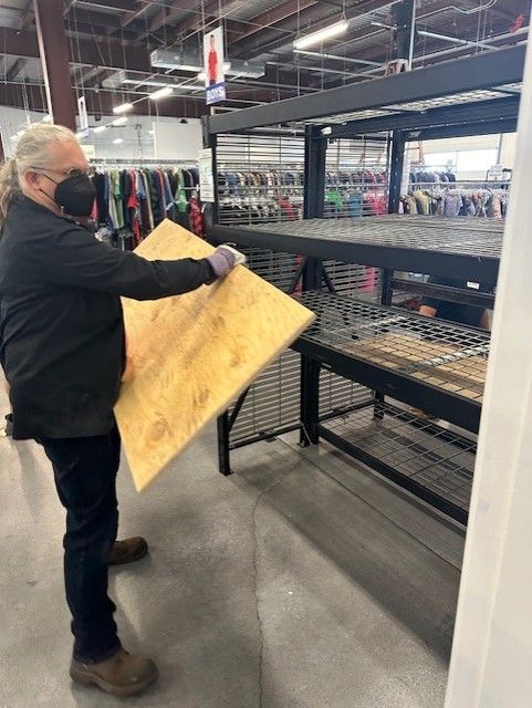 Man in mask placing a plywood shelf into a metal retail display rack.