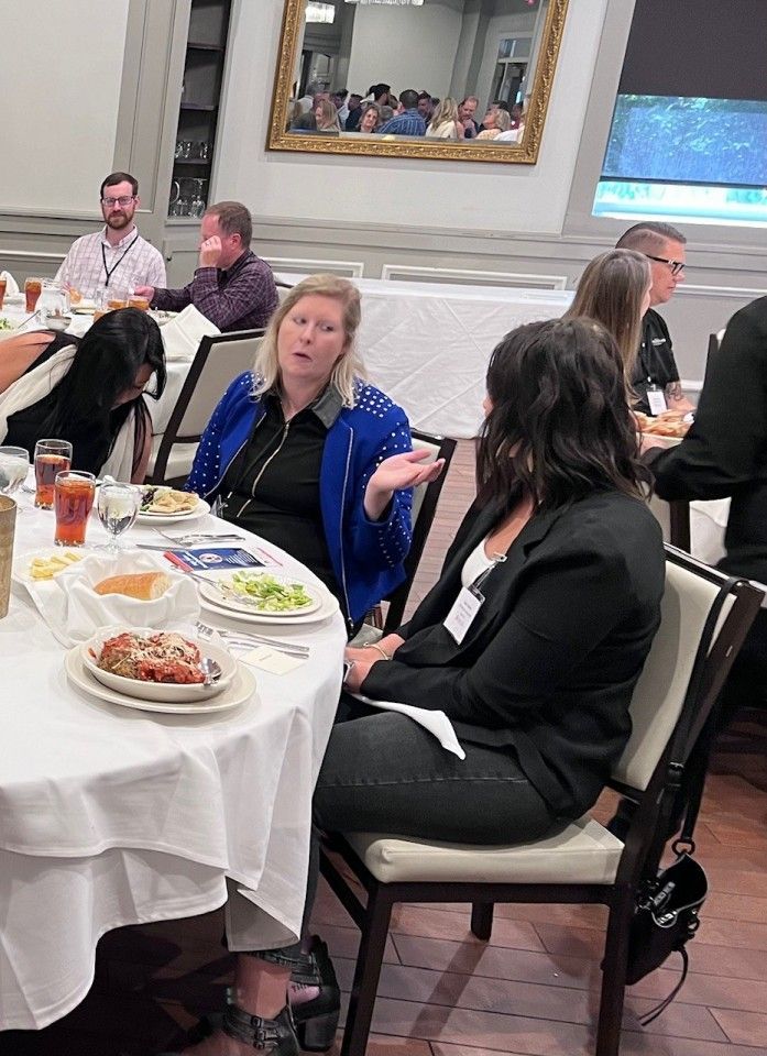 People at a round table, one woman gestures as she speaks to another in a business setting.