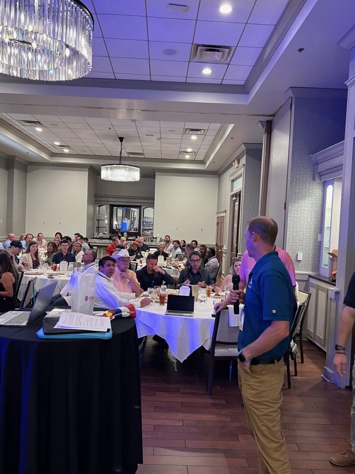 Conference room with a speaker addressing a seated audience at round tables.