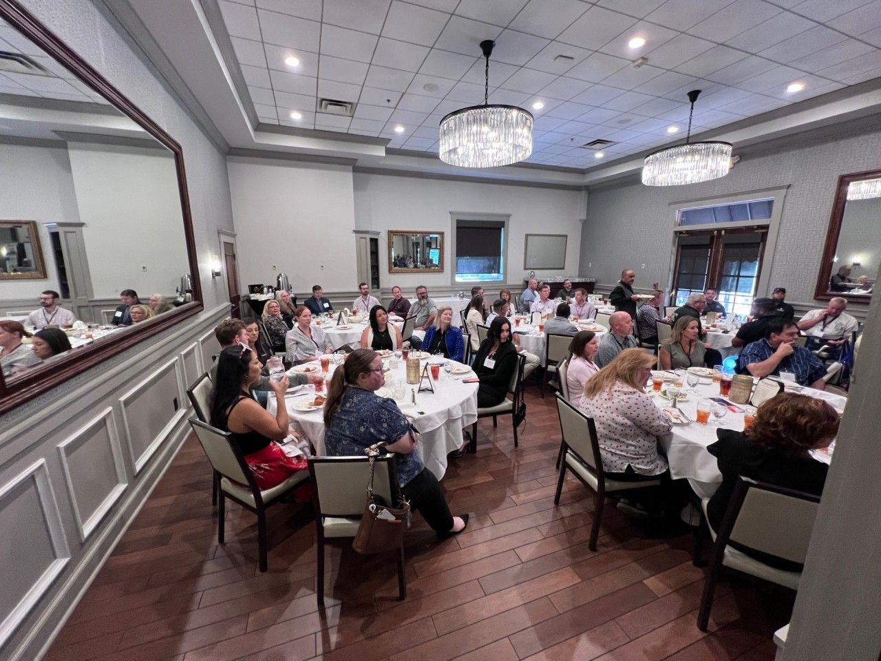 A large group of people seated at round tables in a banquet hall, possibly attending an event or conference.