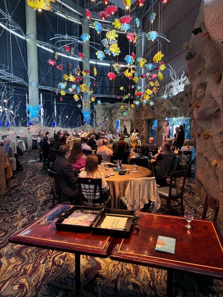 Restaurant with people seated at tables, colorful fish decorations hanging from the ceiling, and rock wall.