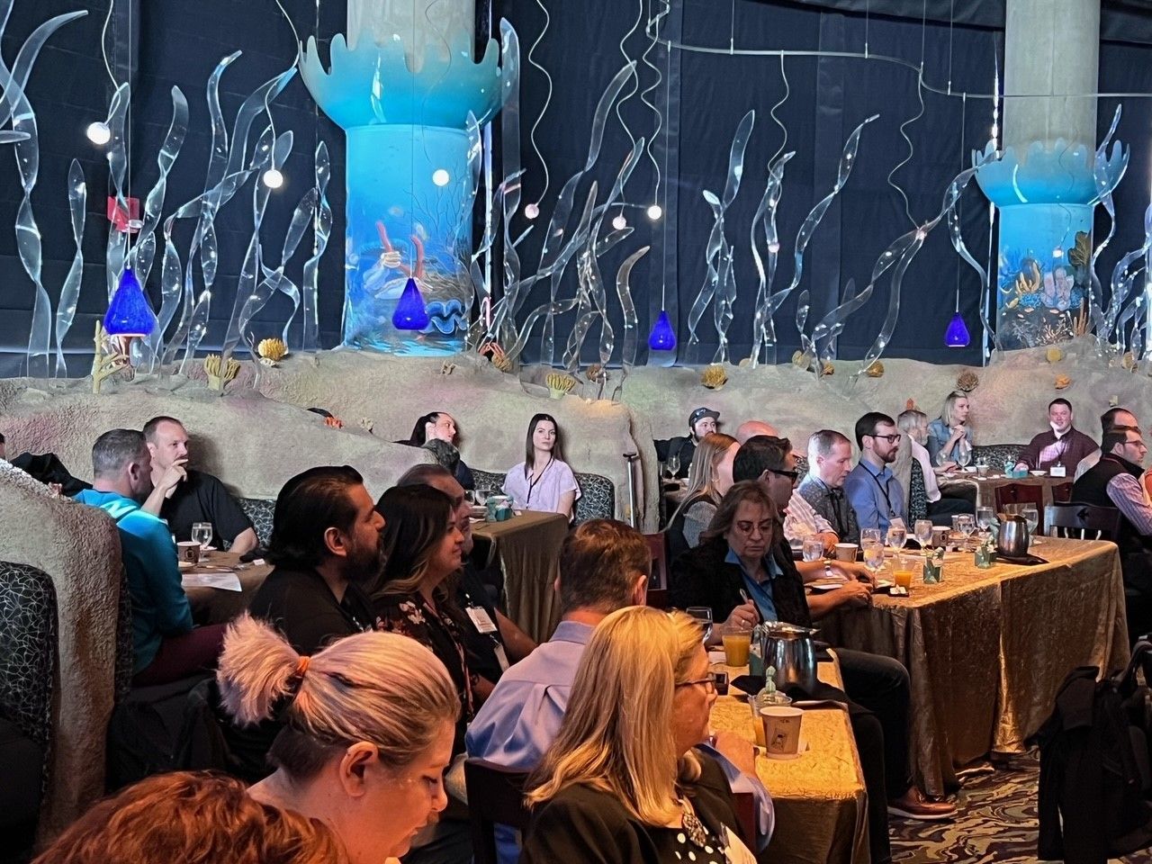 A group of people seated at tables in a restaurant with aquatic-themed decorations.