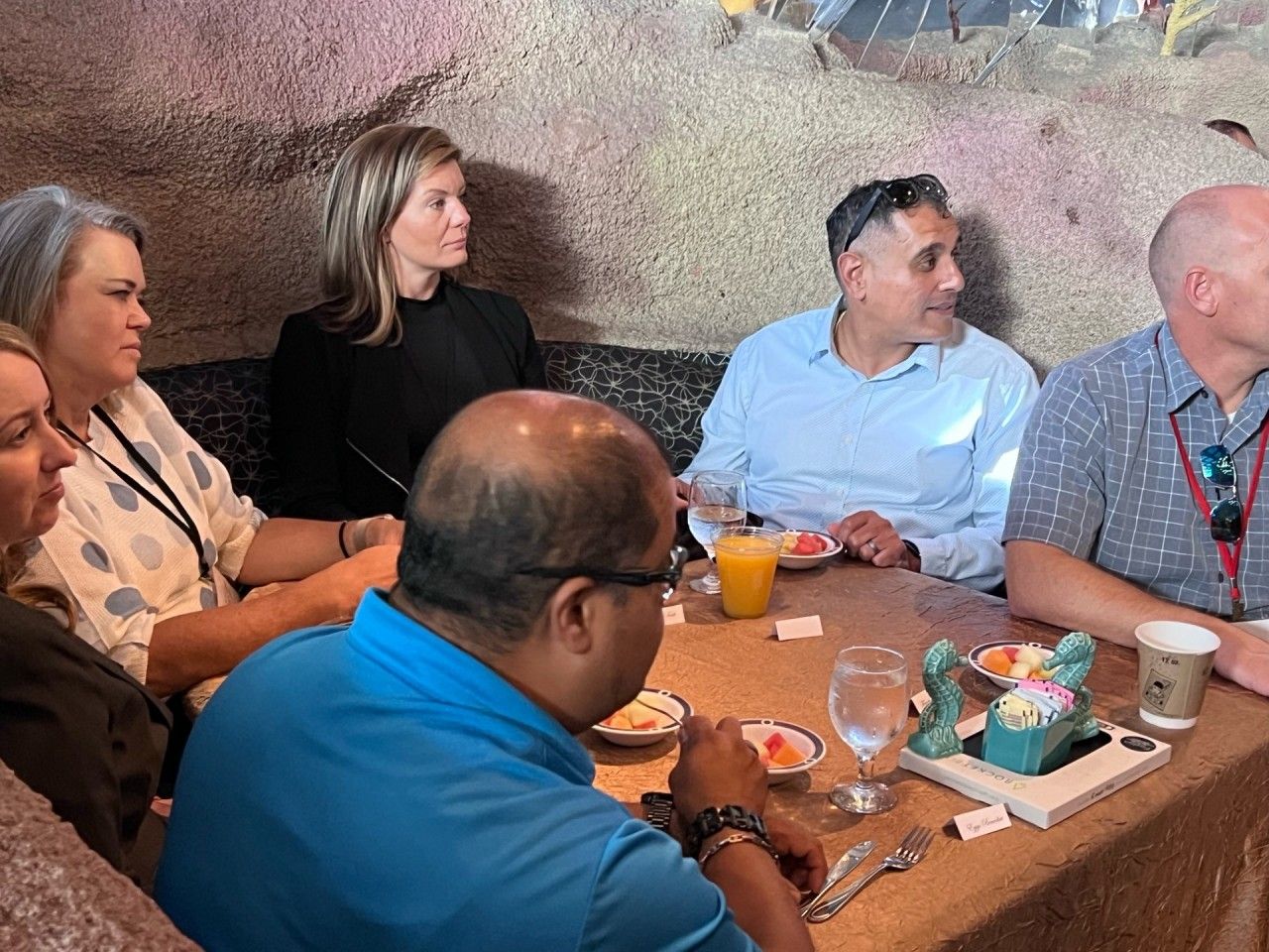 People seated around a table in a restaurant; some eating, some looking to the right.