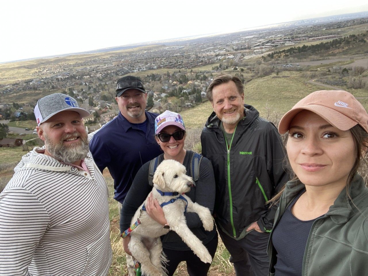 Group of five people and a dog posing for a photo on a hilltop overlooking a town.