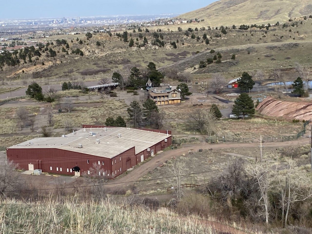 Brown buildings and sparse trees on a hillside overlooking a city, under a cloudy sky.