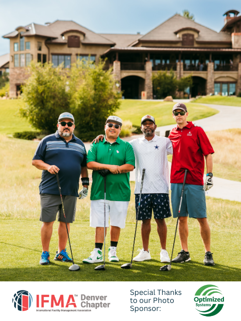 Four men on a golf course holding clubs, posing for a photo. A large building in the background.